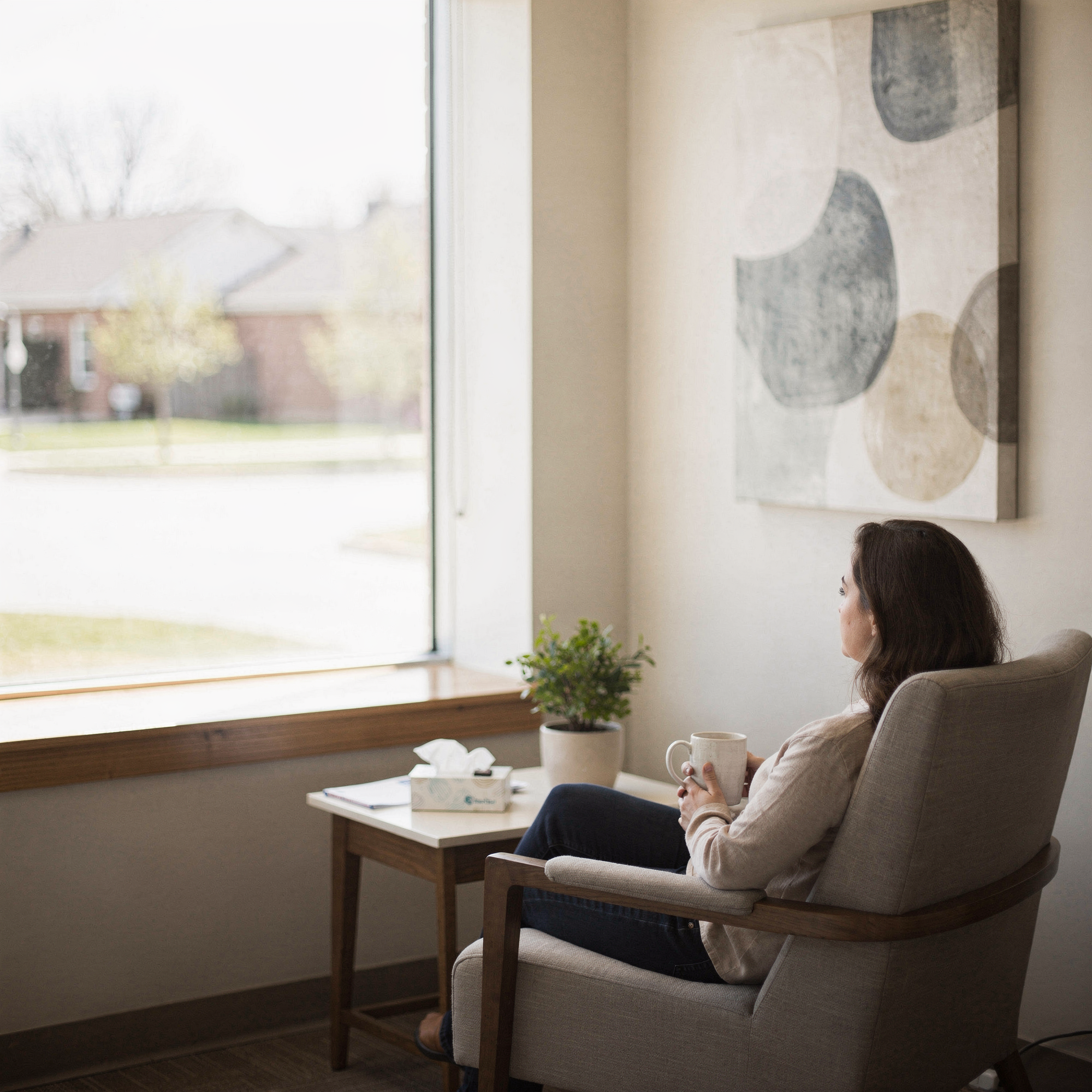 Woman sitting in a comfortable chair holding a mug in a calm clinical waiting room with a window view